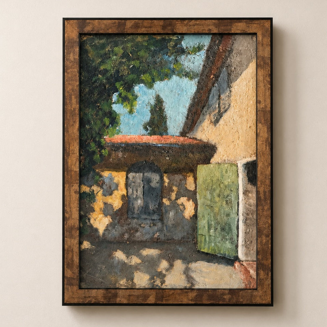 A framed painting of a rustic courtyard scene with a beige building, green shutters, a red-tiled roof, and a tree, displayed on a light beige wall.